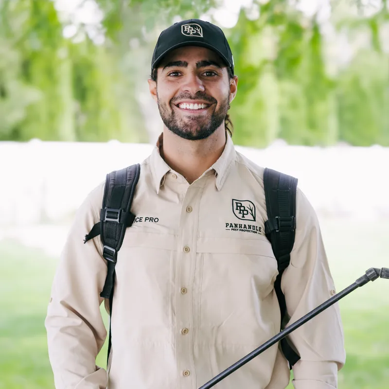 Smiling Panhandle Pest Protection technician in uniform with a backpack sprayer and wand on a lawn
